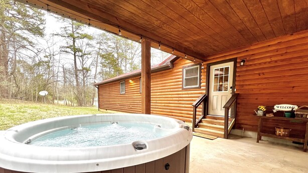 Een houten blokhut met een jacuzzi, een houten trap en een welkomstbord.