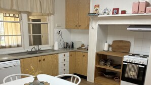 Une cuisine compacte avec des meubles en bois, un plan de travail blanc, une cuisinière et un coin repas comprenant une table et des chaises blanches.
