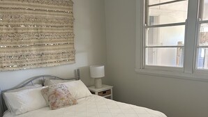 Un lit bien fait, avec un cadre en métal, une table de chevet avec une lampe et une grande fenêtre donnant sur l’extérieur.