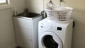 Un espace buanderie compact comprenant un lave-linge, un sèche-linge, une fenêtre et une prise de courant au mur.