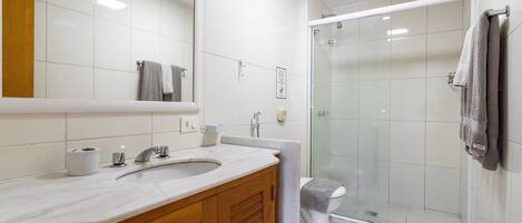 A modern bathroom with a marble sink, wooden vanity, a glass shower enclosure, and a toilet.