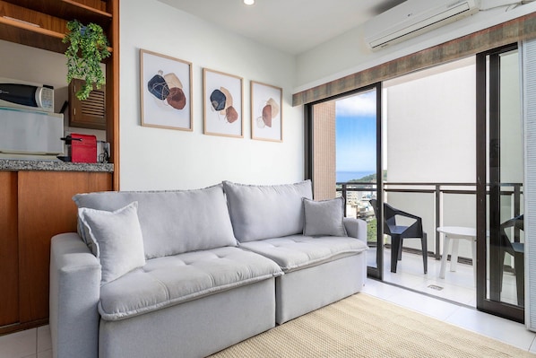 A modern living room with a grey sofa, a small table, and a balcony with a view.