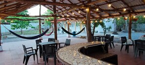 Patio esterno con un bancone in pietra curvo, sedie in plastica nera e amache.