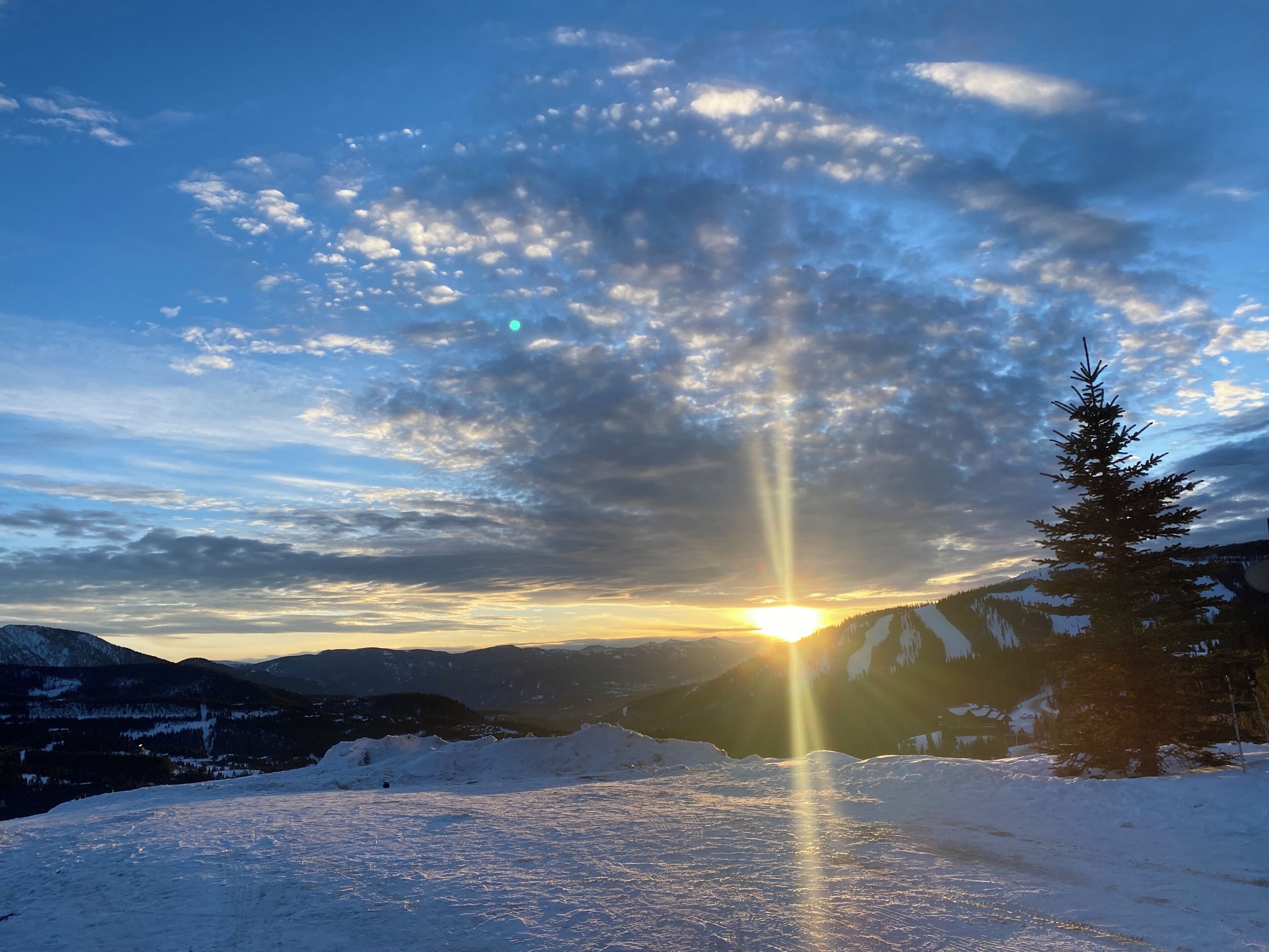 A snowy mountain landscape with a clear sky and the sun shining through the clouds.