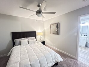 Ein Schlafzimmer mit einem Bett, einem Deckenventilator, einem Nachttisch mit Lampe und einem Bild an der Wand.