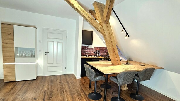 A modern kitchen with a wooden ceiling beam, a dining table with chairs, and a kitchen island with a coffee machine.