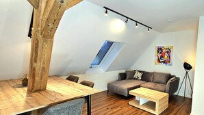 A modern loft-style room with a wooden dining table, a gray sofa, and a small wooden coffee table.