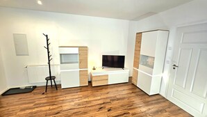 A modern, well-lit room with a wooden floor, white furniture, a coat rack, a TV, and a door.