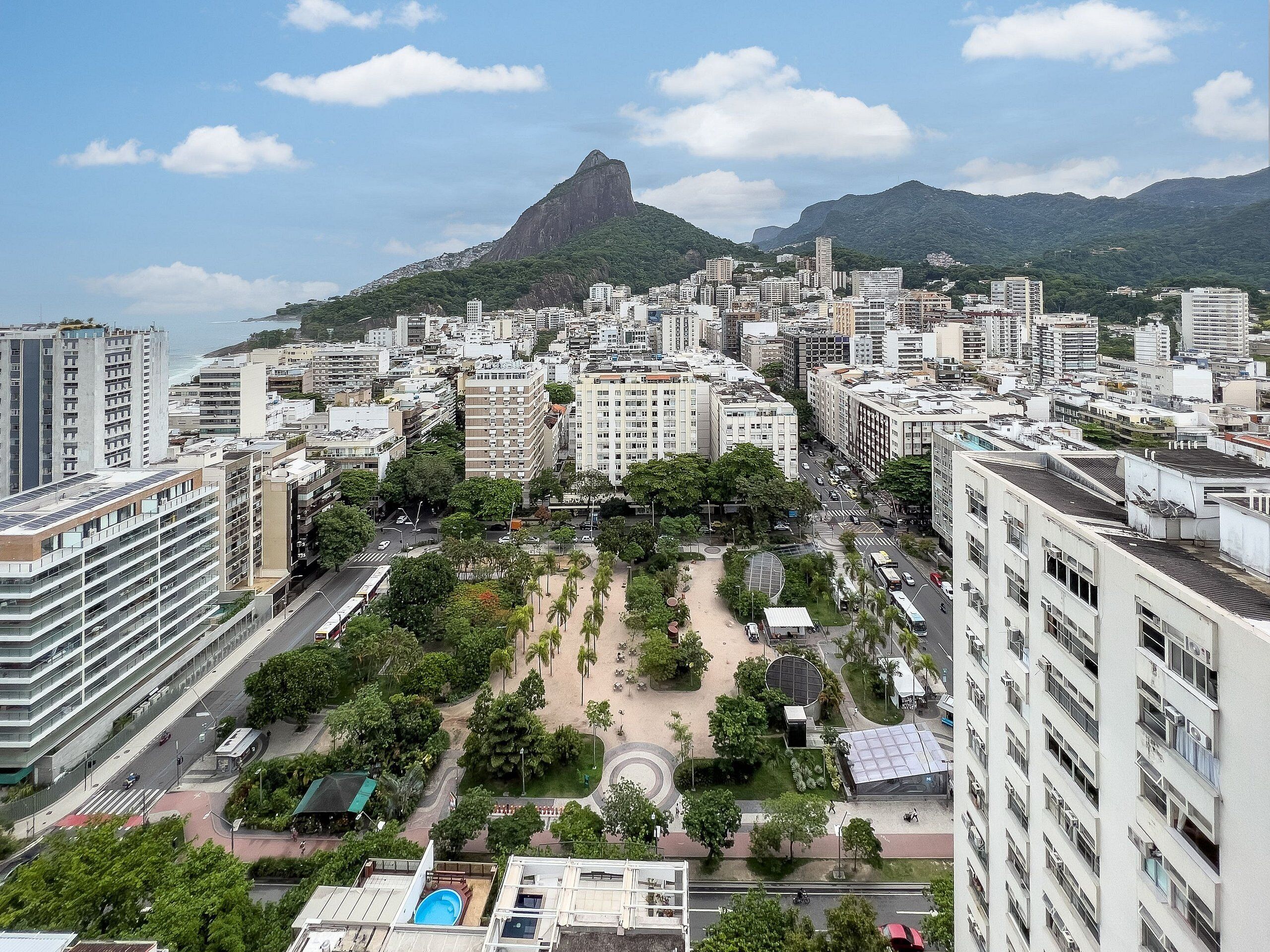 A cityscape with modern buildings, a prominent mountain in the background, and a central park area.