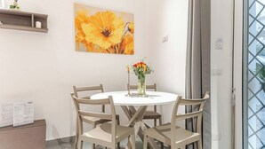Un coin repas avec une table ronde, six chaises, un vase de fleurs et un tableau au mur.