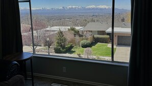 Une pièce dotée d’une grande fenêtre donnant sur un quartier résidentiel, avec des montagnes visibles au loin.