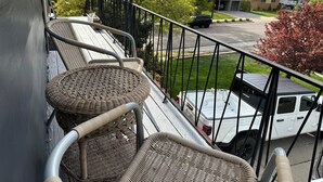 Un balcon avec des fauteuils en osier et une vue sur un parking et des maisons.