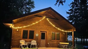 Eine Holzhütte mit Veranda, zwei Stühlen, einer Bank und einem Grill.