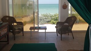 A room with a bed, two wicker chairs, a small table, and a view of the ocean through large glass doors.