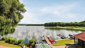 Une vue sur le lac, avec des bateaux amarrés à un quai, le tout entouré d’une végétation luxuriante et sous un ciel dégagé.