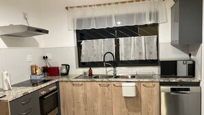 A kitchen with a stainless steel dishwasher, a microwave, a sink, and a window with a curtain.