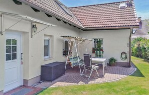 A house with a patio area featuring a swing set, a table, and chairs.