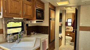 Cocina compacta para autocaravana con fregadero, estufa, microondas y armarios de madera.