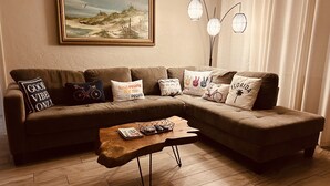 En stue med en hjørnesofa, et sofabord, et billede på væggen og en gulvlampe.