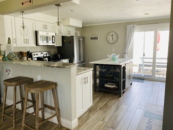 A modern kitchen with white cabinets, stainless steel appliances, a central island with stools, and a view to the outside.