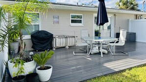 En overdækket terrasse med et bord og stole, omgivet af krukker med planter og en grill.