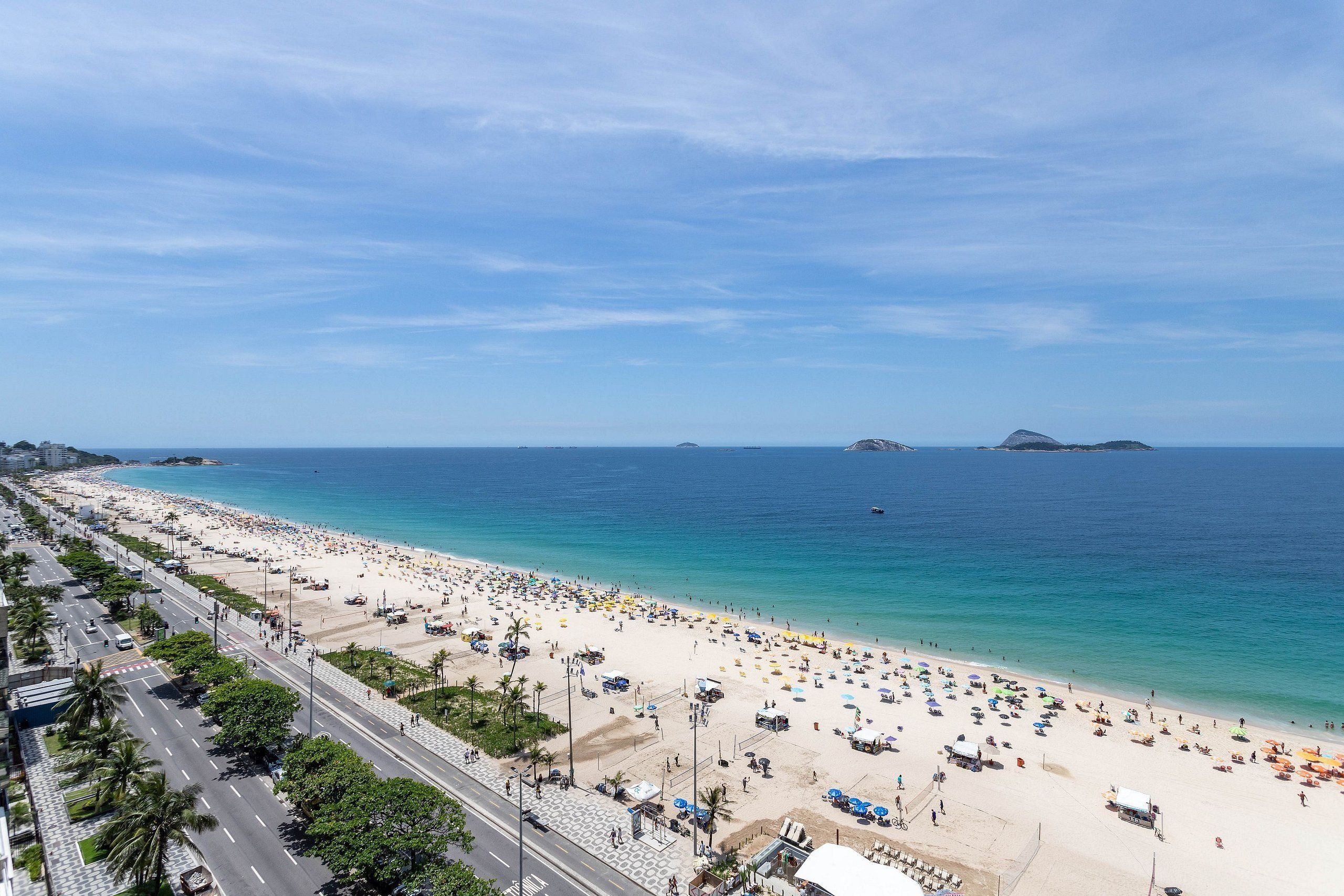 A beach with a road running parallel to it, a clear sky, and calm sea.