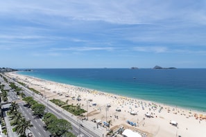 Une plage bordée d’une route qui la longe, un ciel dégagé et une mer calme.