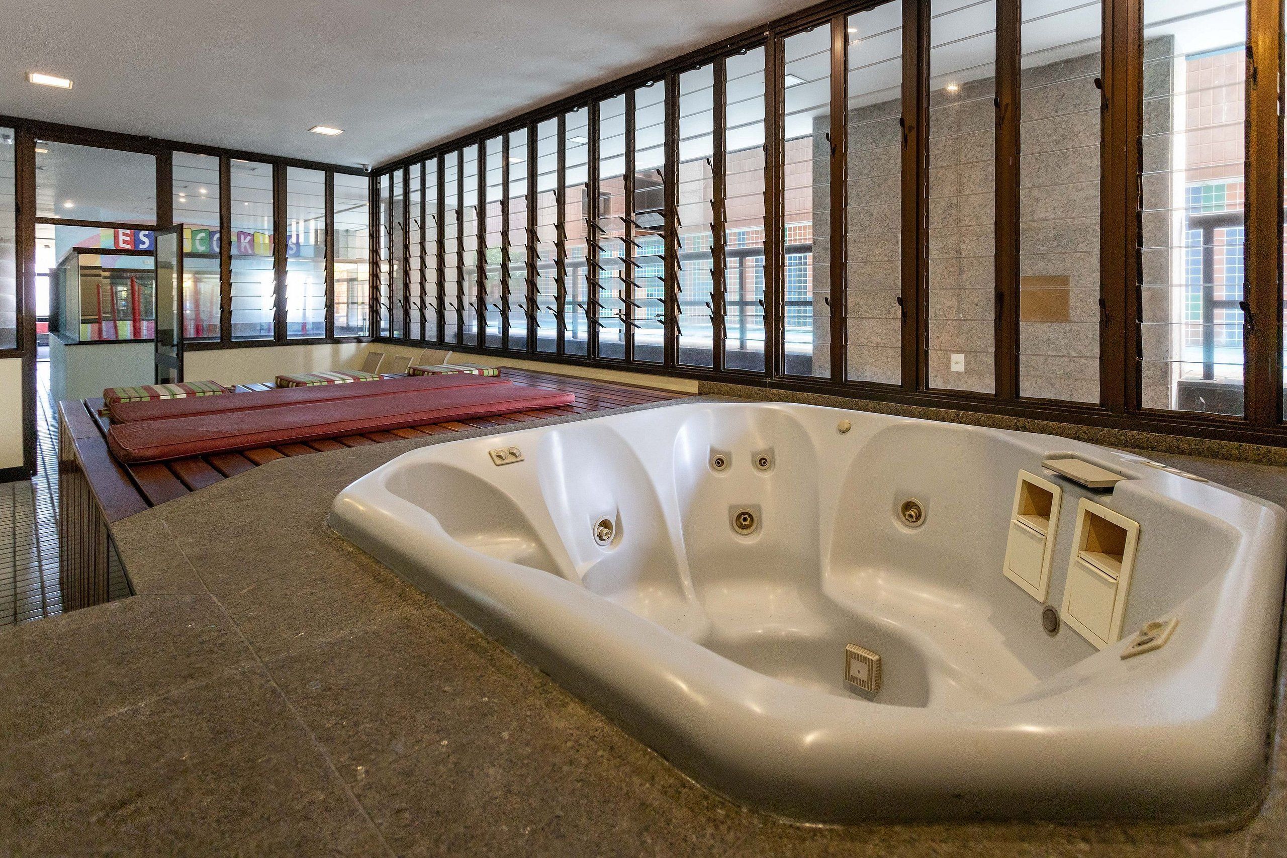 A spa area with a large hot tub, wooden benches, and a view through a window with a metal grid.