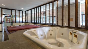 A spa area with a large hot tub, wooden benches, and a view through a window with a metal grid.