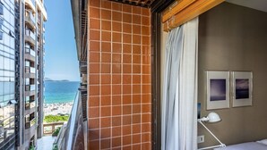 Une chambre d’hôtel avec un balcon donnant sur une plage et l’océan, un lit avec un oreiller blanc et une table de chevet avec une lampe.
