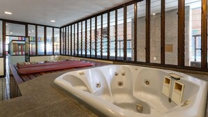 Un espace spa comprenant un grand jacuzzi, une table de massage et une vue à travers une paroi en verre.