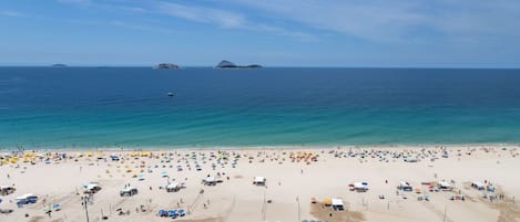 A beach with numerous umbrellas and people, a clear sky, and distant islands.