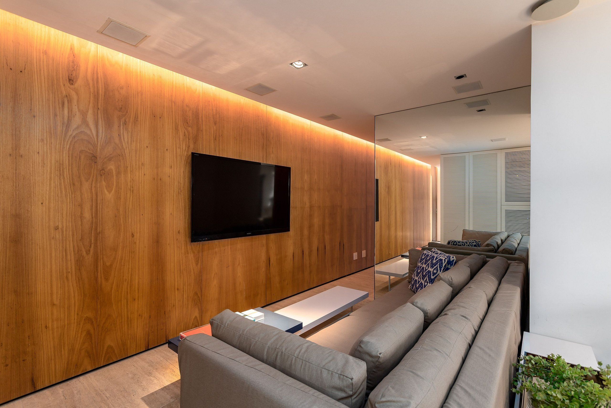 A modern living room with a flat-screen TV mounted on a wooden wall, a sectional sofa, and a small coffee table.
