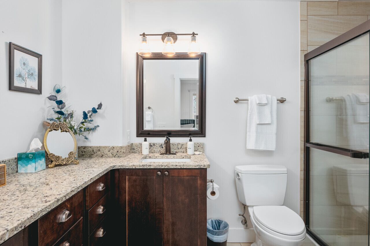 A bathroom with a granite countertop, a wooden vanity, a white toilet, and a glass shower enclosure.