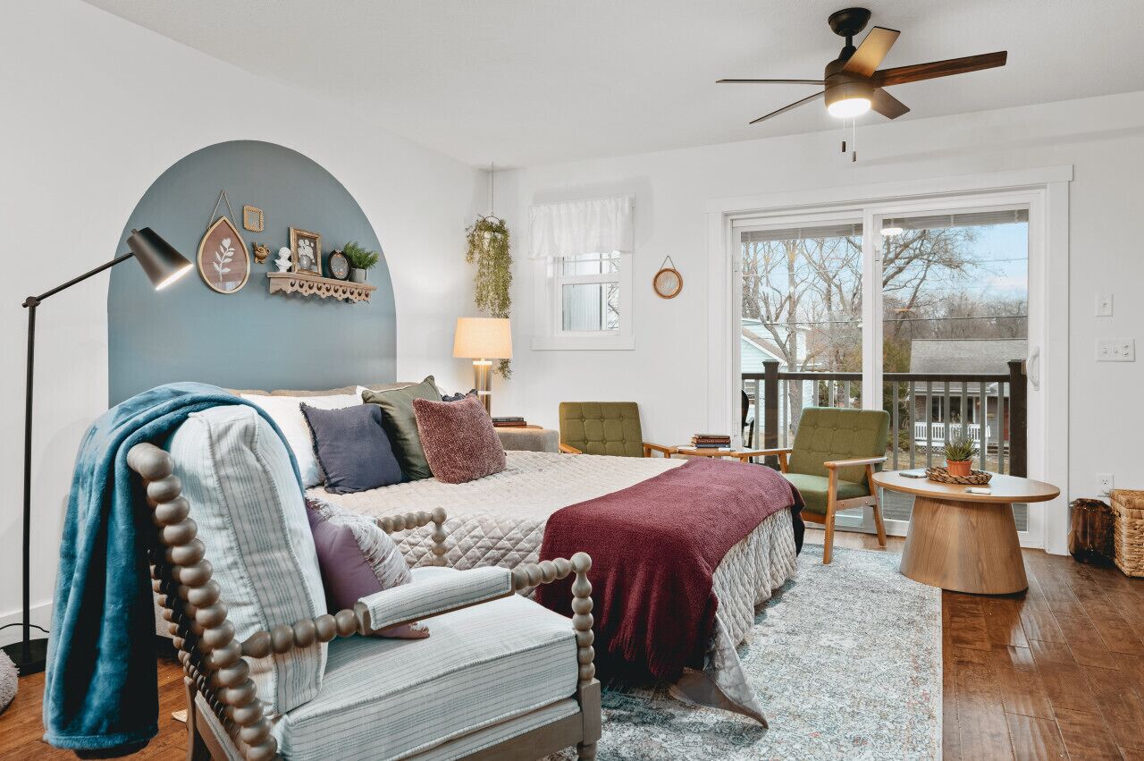 A bedroom with a bed, a chair, a table, a lamp, and a ceiling fan.
