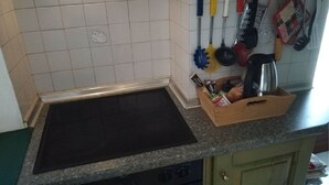 Uma cozinha com um fogão por indução preto, um suporte de madeira para temperos e diversos utensílios de cozinha.