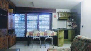 Uma sala de estar com sofá, mesa de jantar com cadeiras e cozinha com armários e bancada.