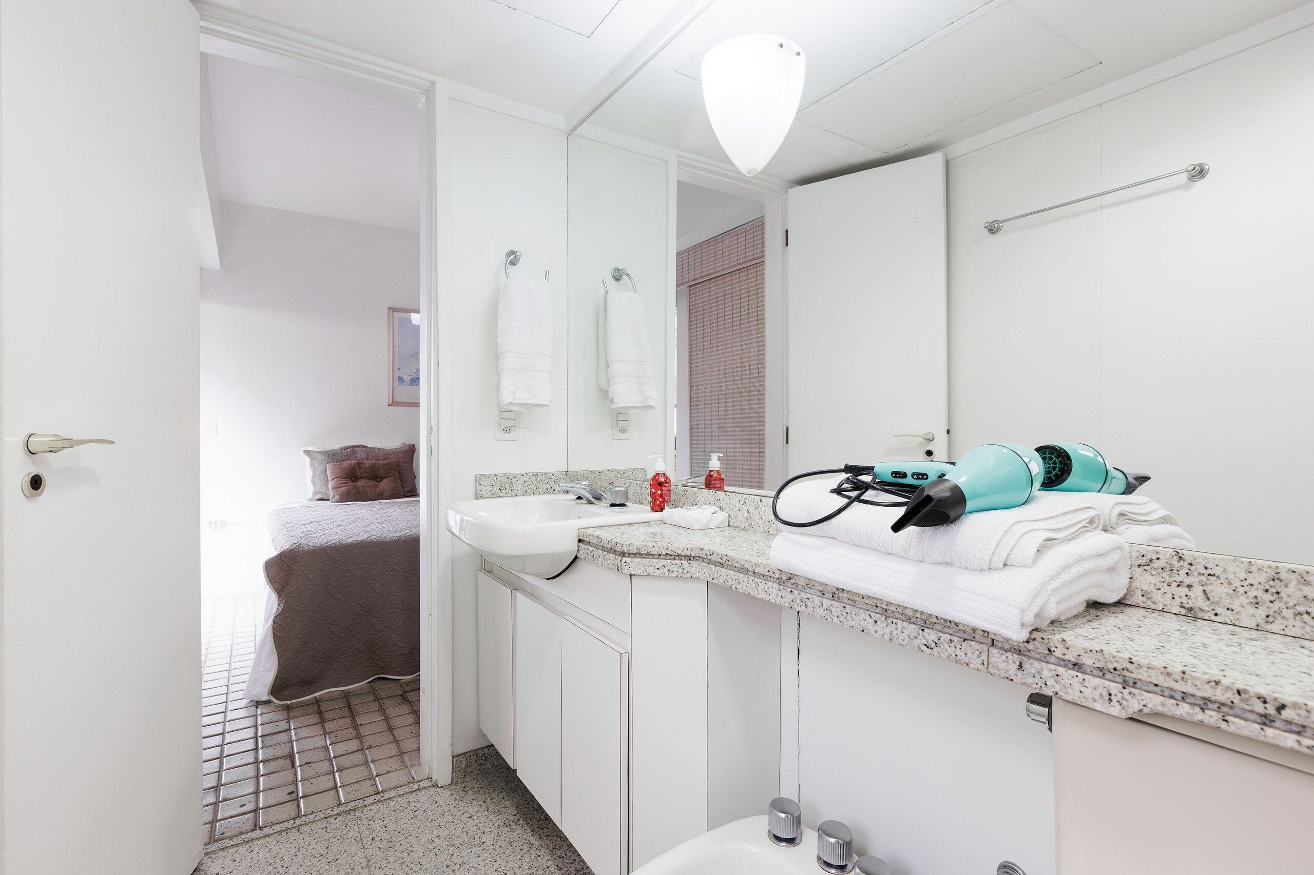A modern bathroom with a white sink, a large mirror, and a hairdryer on the counter.