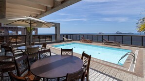 A pool area with lounge chairs and a table, overlooking a body of water. - 802 (Rio de Janeiro)