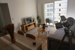 Relax in this stylish living room with a sofa set, coffee table, and TV on a stand, plus a balcony with a chair and table.