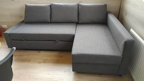 A grey sectional sofa with a chaise, a wooden floor, and a radiator on the wall. - Brekkukot Cottage  (Blönduós)