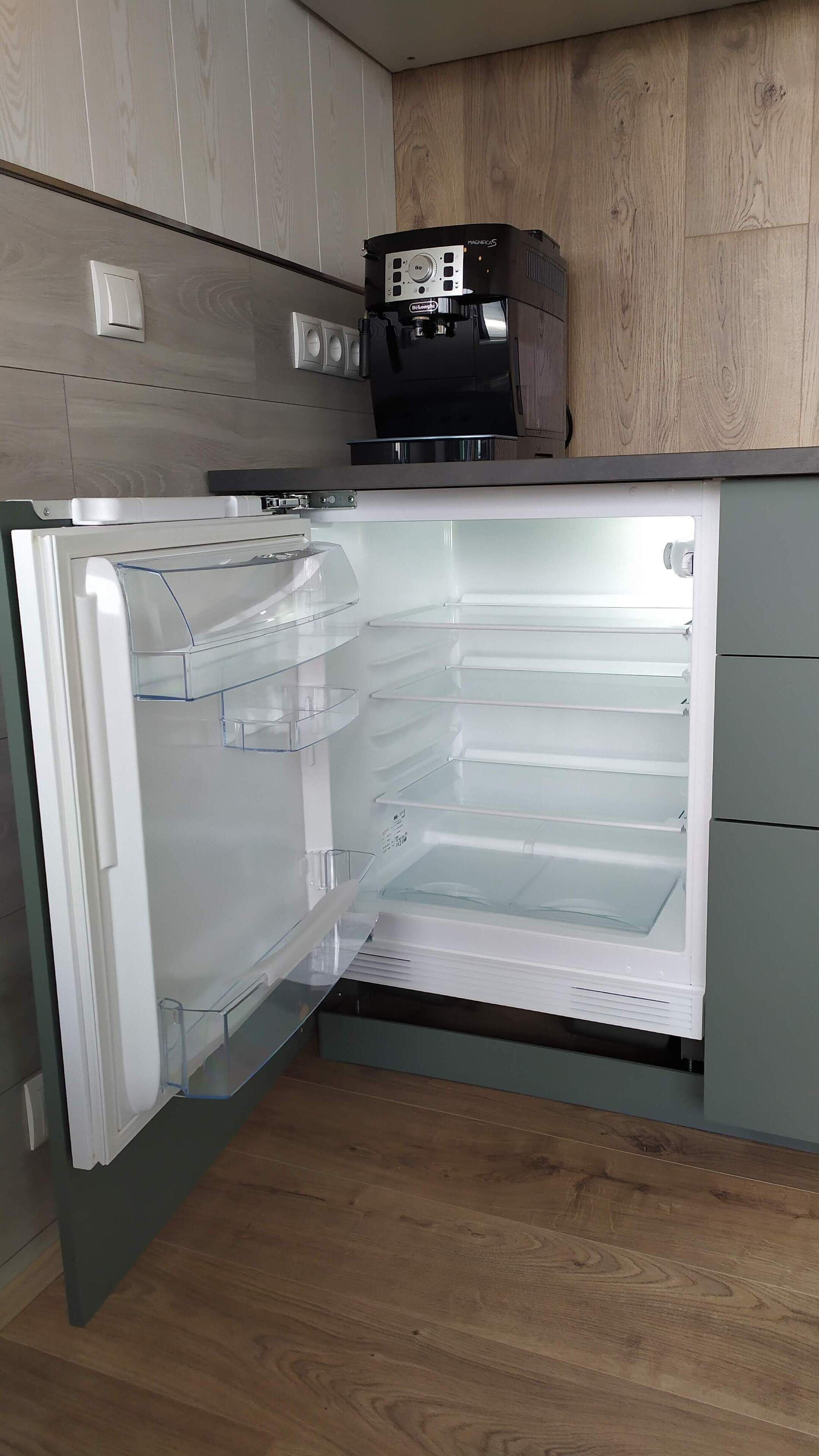 Ein offenes Kühlschrank mit klaren Regalen und einer Kaffeemaschine darauf.