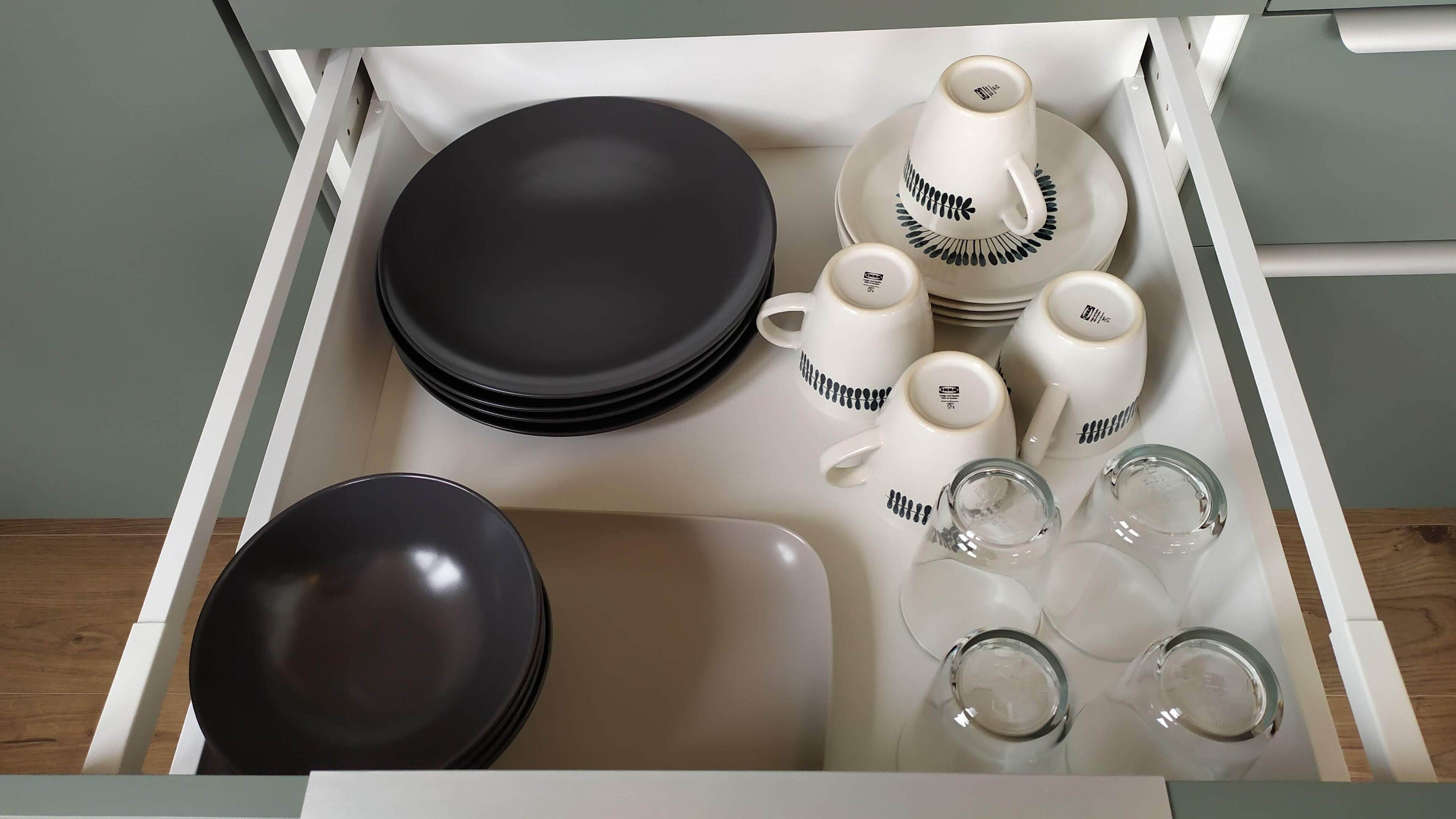 A drawer containing black and white plates, bowls, and glassware.