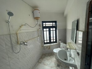 A bathroom with a toilet, sink, and shower. There is a window with bars, and the walls are tiled.