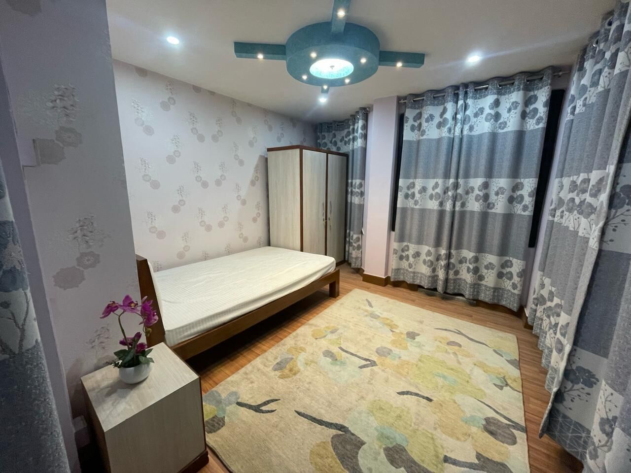 Een slaapkamer met een bed, een kledingkast, een tafeltje met een plant en een kamerbreed tapijt.