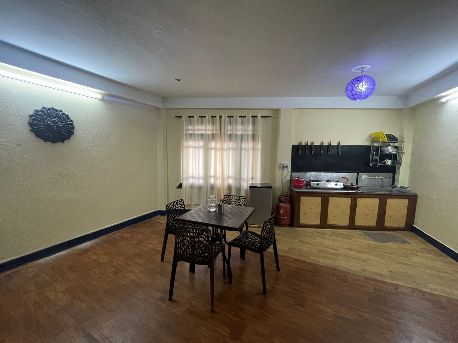 Een kleine, functionele ruimte met een eethoek, kitchenette en een klein raam met gordijnen.