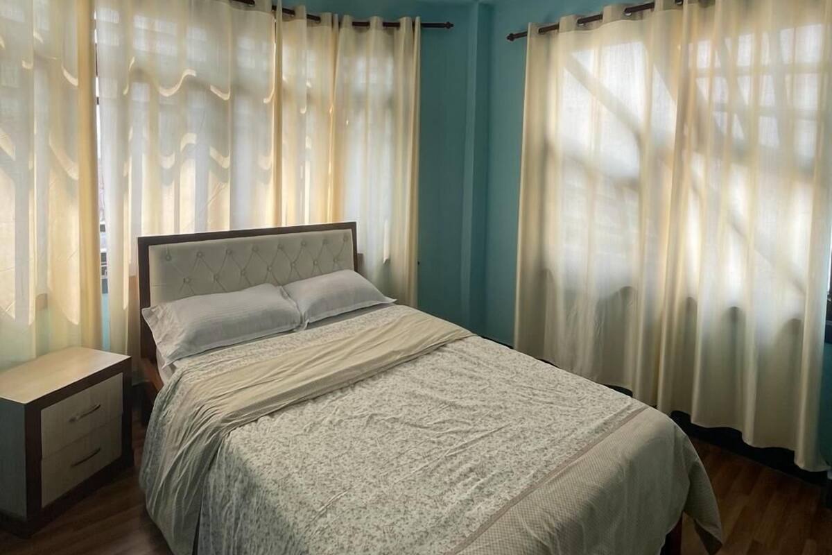 A bedroom with a bed, curtains, a nightstand, and a wooden floor.
