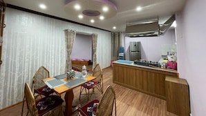 A compact kitchen with a central island, a dining area with a table and chairs, and a modern ceiling light fixture. - Dzambala Apartment (Kathmandu)