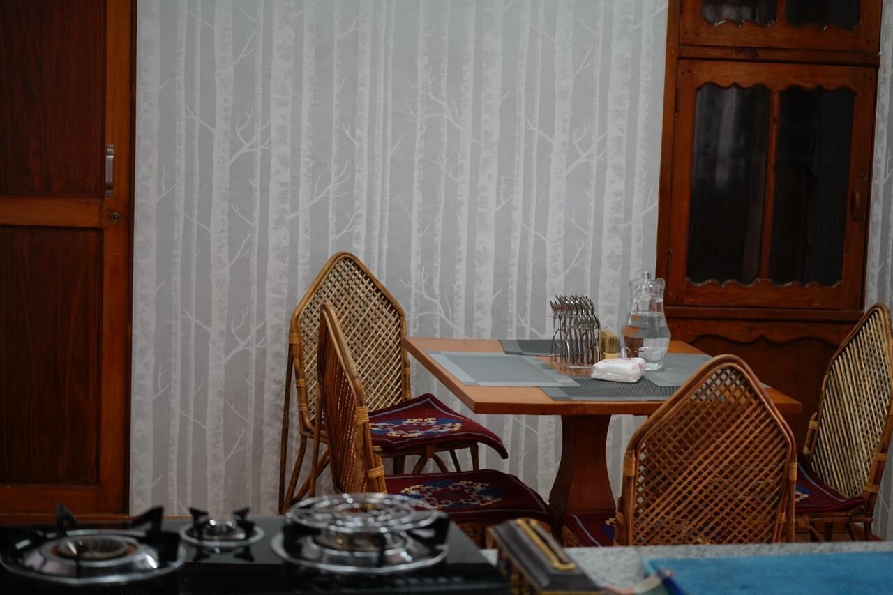 A dining area with a table set for two, surrounded by wicker chairs. A wooden cabinet with glass doors is visible in the background.