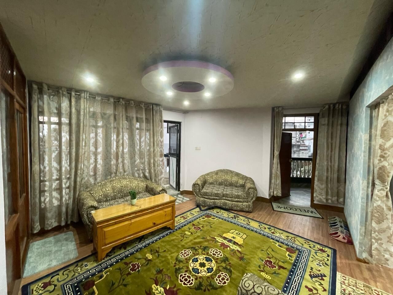 A living room with a sofa, a wooden coffee table, a patterned rug, and curtains.